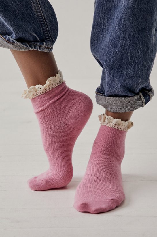 Woman wearing pink ankle sock with lace trim on plain background