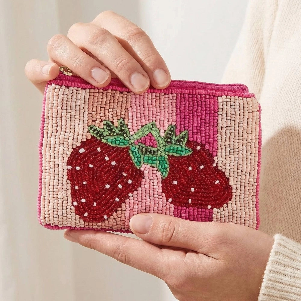 Hand holding a pink beaded pouch with strawberry design against a neutral background