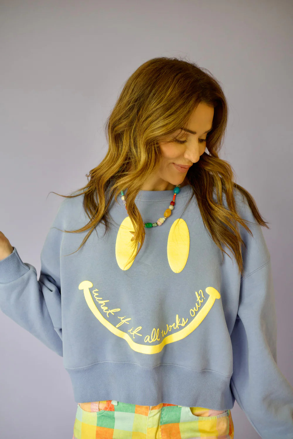 Woman wearing purple crewneck with smiley face on plain background