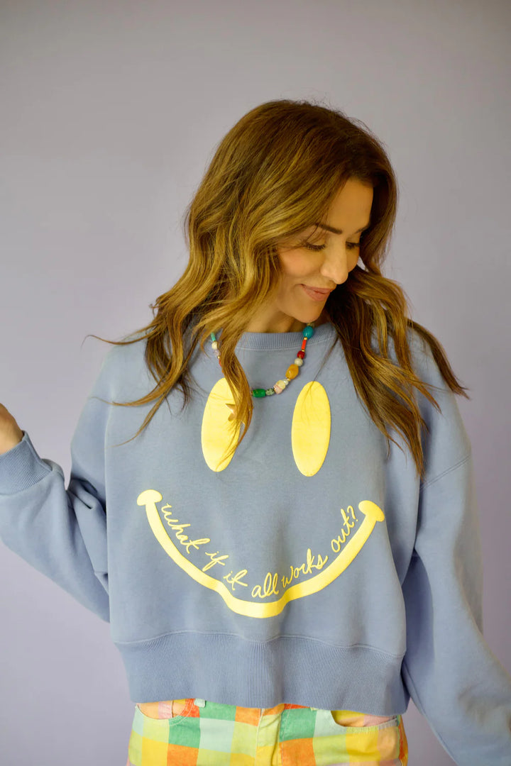 Woman wearing purple crewneck with smiley face on plain background
