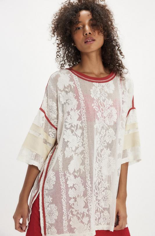 Woman wearing a white lace top with red accents on a plain background