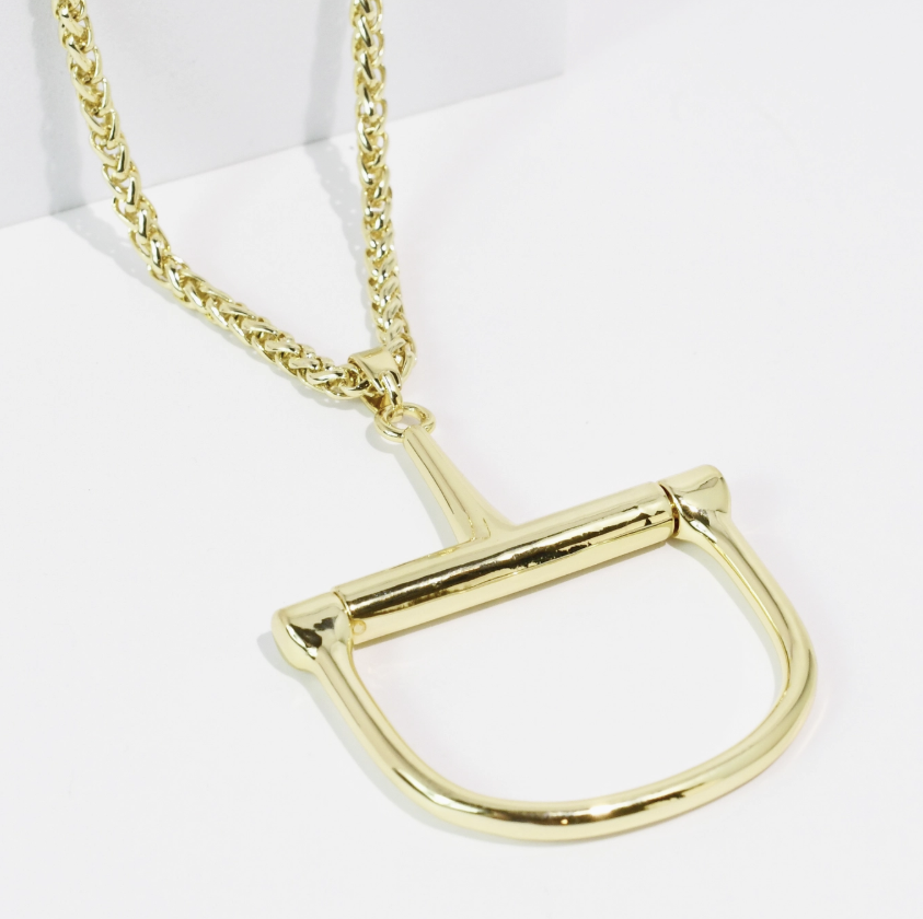 A gold-tone horsebit necklace with a thick curb chain, displayed on a clean white background.