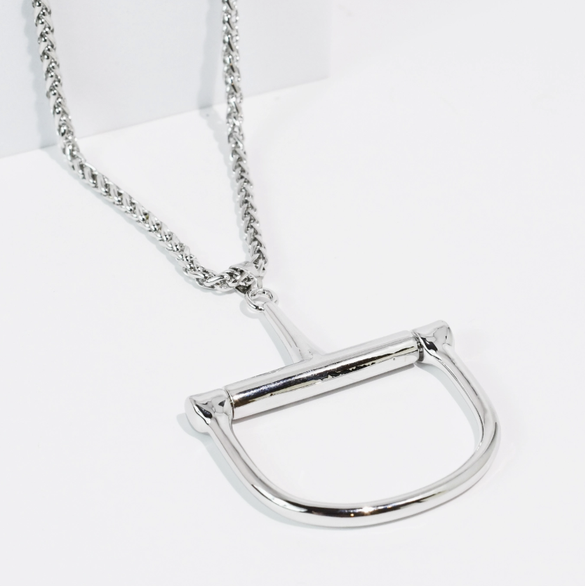 A silver-toned metal necklace featuring a large, polished horsebit-shaped pendant on a matching chain, displayed on a clean white background.