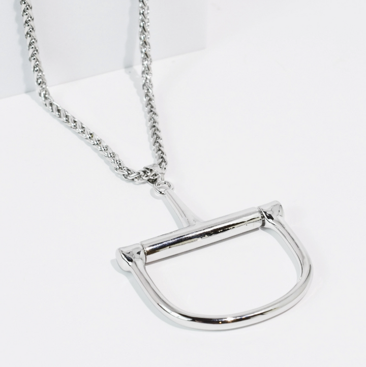 A silver-toned metal necklace featuring a large, polished horsebit-shaped pendant on a matching chain, displayed on a clean white background.