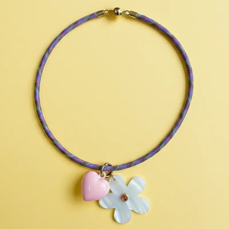 Necklace with a pink heart and white flower pendant on a yellow background