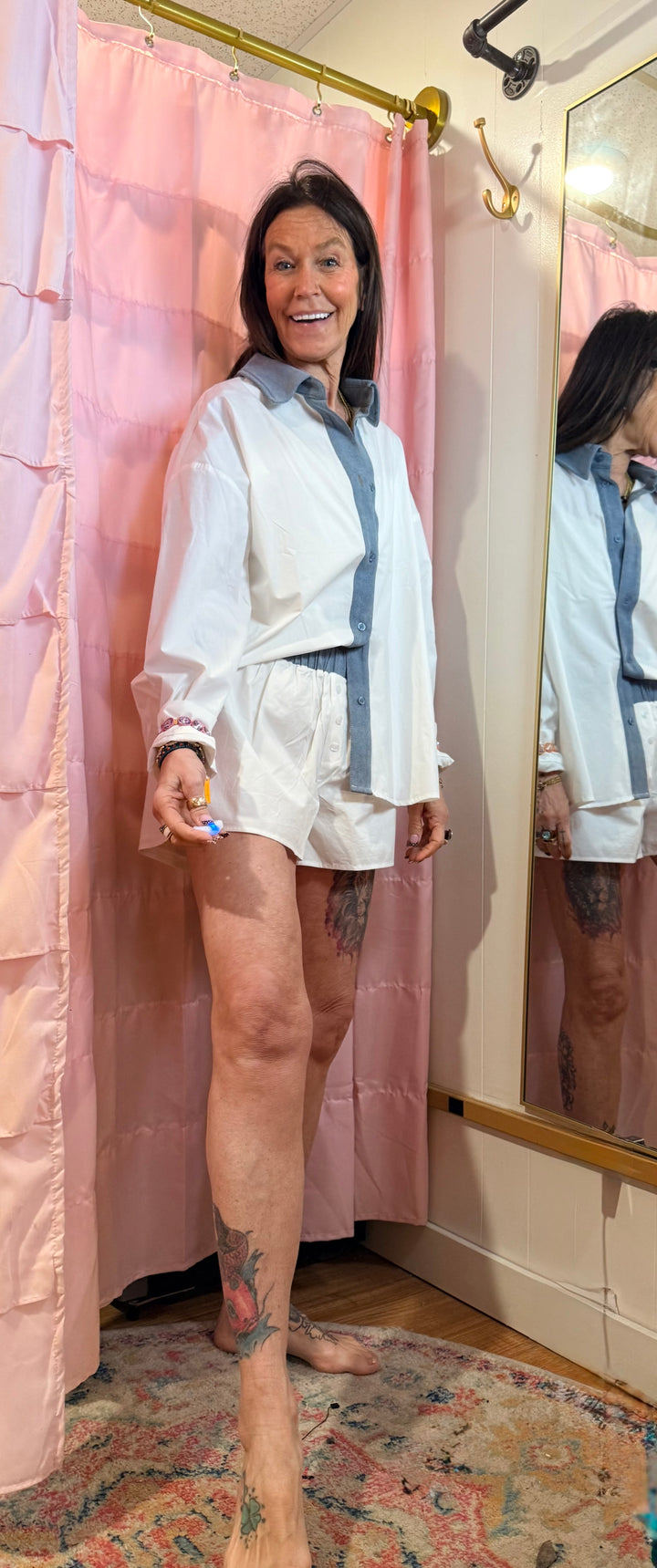 Woman standing in front of a mirror wearing a white outfit with a pink curtain in the background.