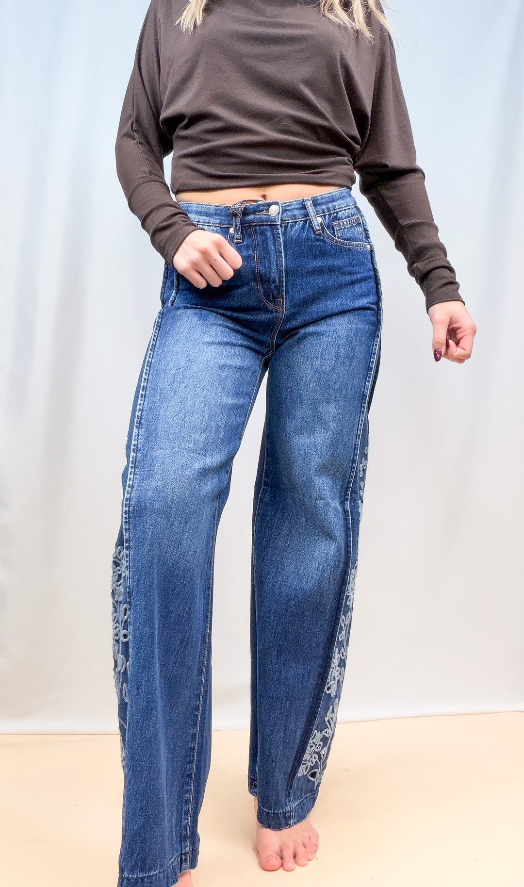 Woman wearing medium wash denim jeans with cutout floral on the sides on plain background