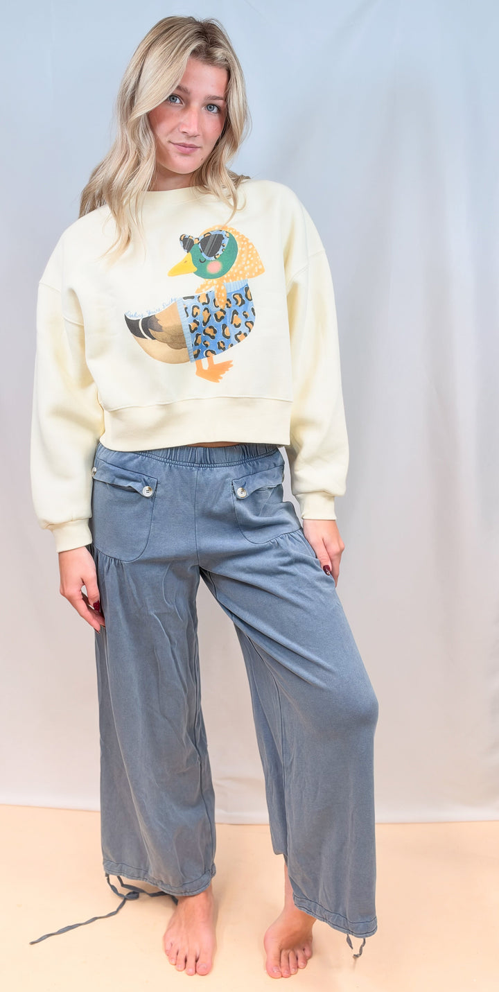 Woman wearing duck graphic sweatshirt with blue cinch hem pants on plain background