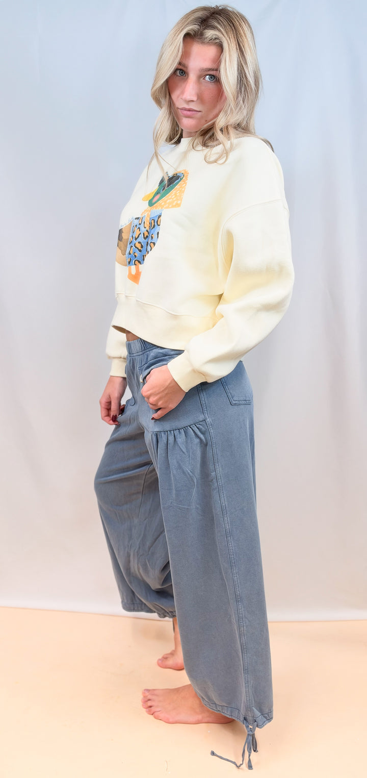 Woman shown from side view wearing duck graphic sweatshirt with blue cinch hem pants on plain background