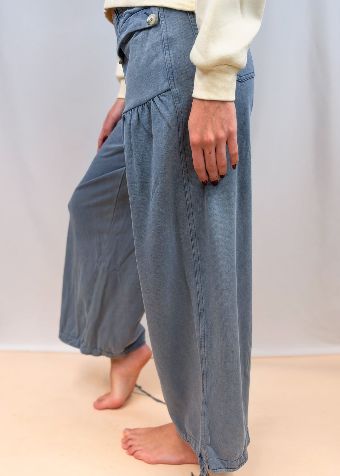 Woman shown from side view wearing blue cinch hem pants on plain background