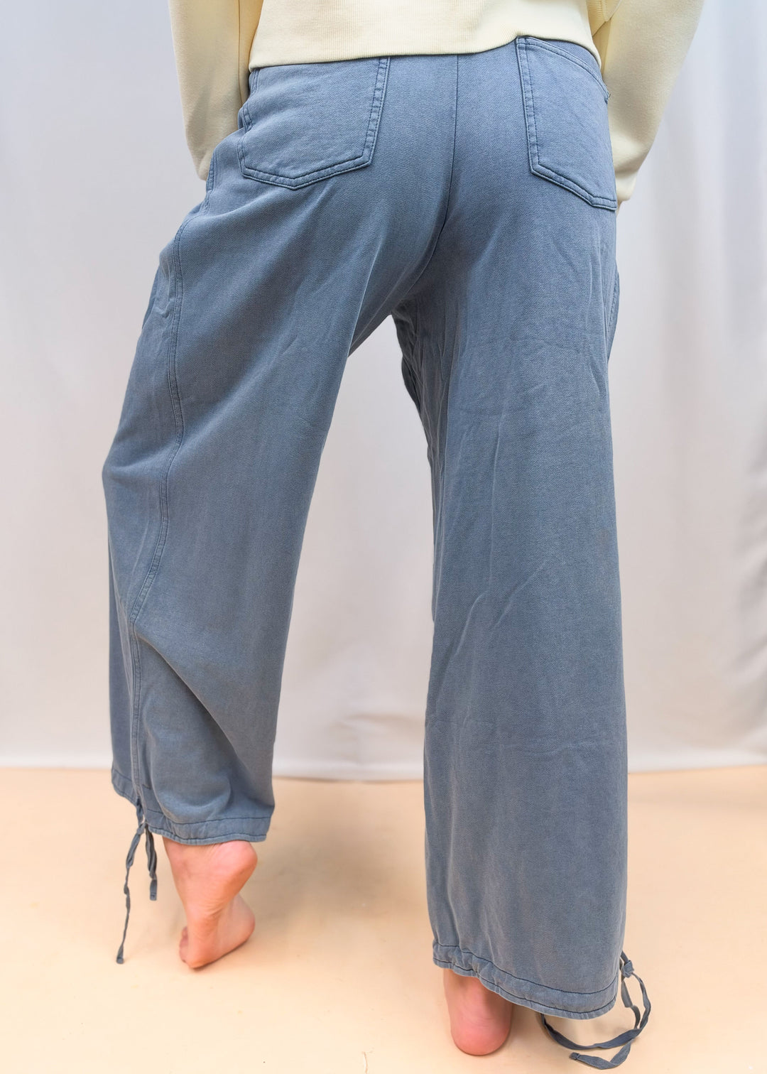 Woman shown from back view waist down wearing blue cinch hem pants on plain background