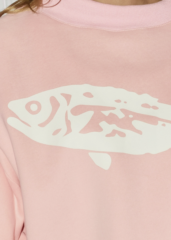 A close-up of a person wearing a light pink crewneck sweatshirt with a large cream-colored fish graphic printed across the chest.