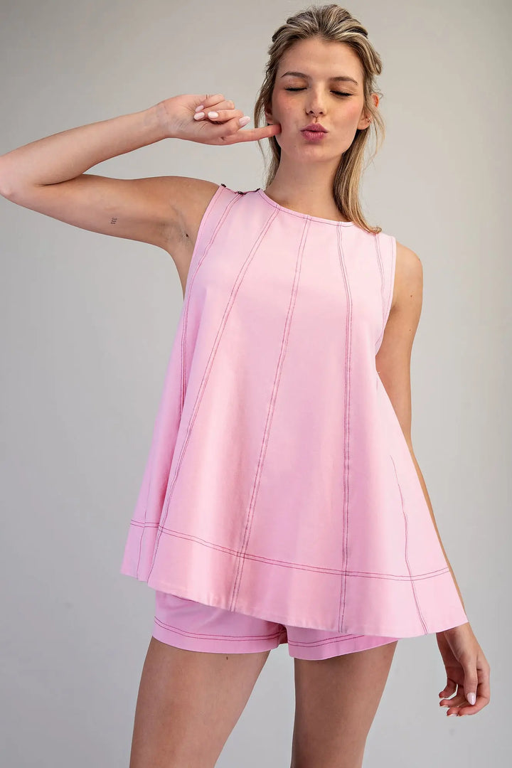 Woman wearing a pink sleeveless top and shorts on a gray background