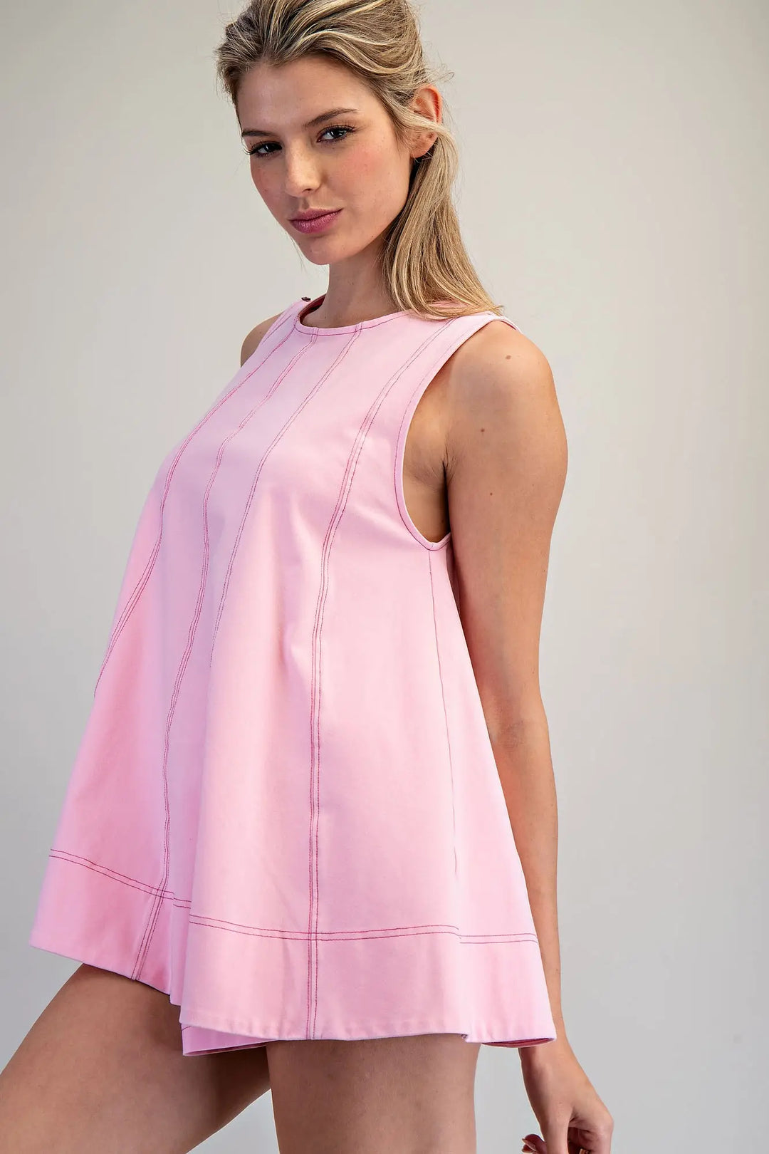 Woman wearing a pink sleeveless dress against a plain background