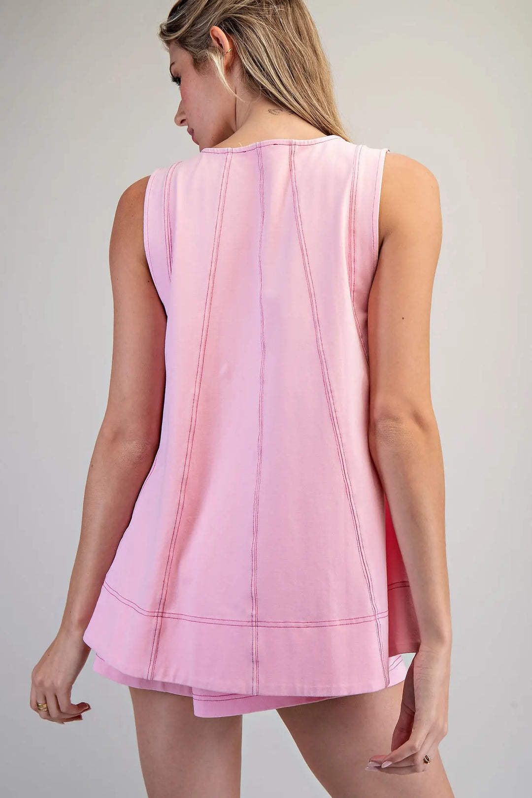 Woman wearing a pink sleeveless top and shorts on a gray background