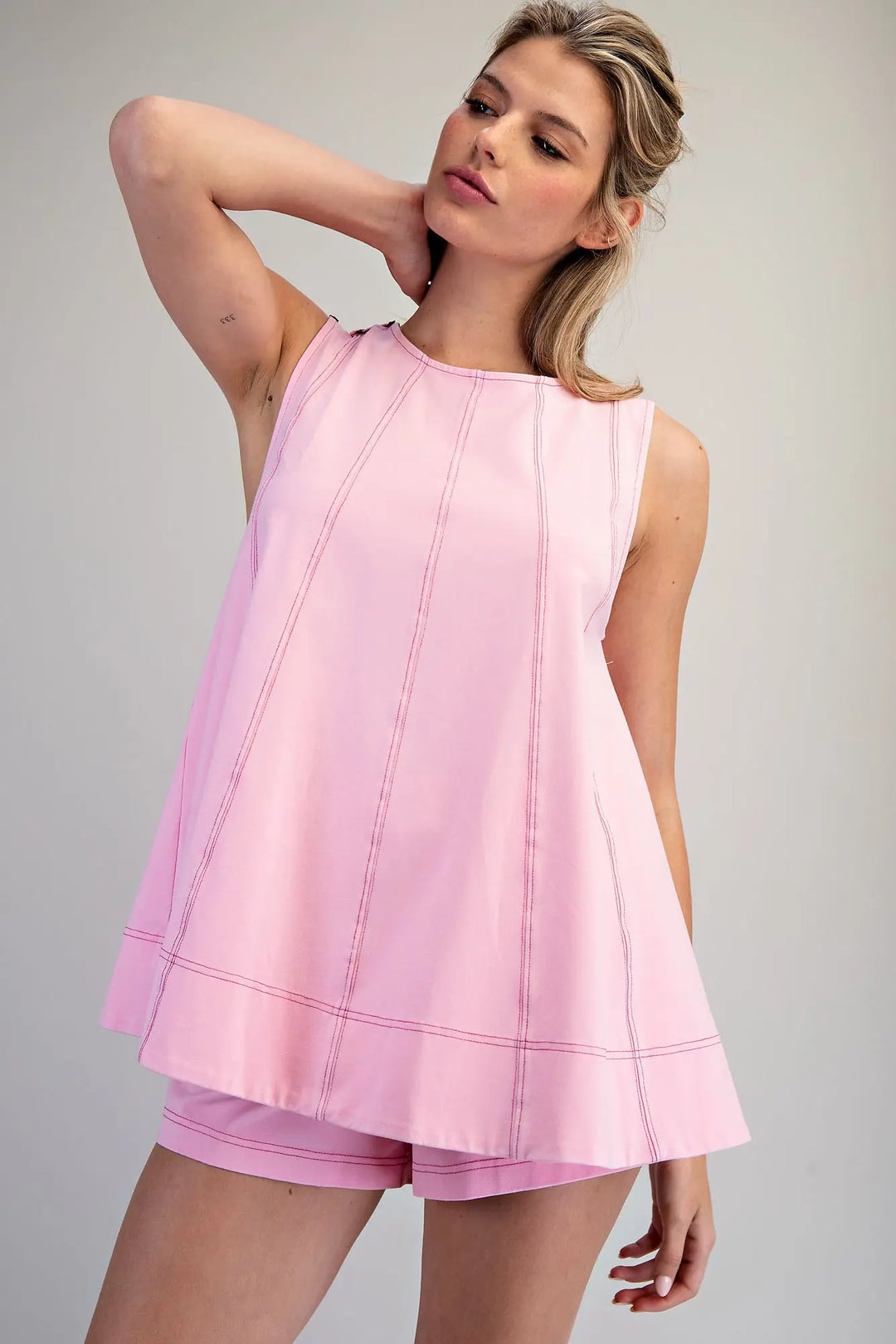 Woman wearing a pink sleeveless top and shorts on a gray background