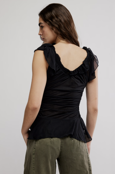 Woman wearing a black top with ruched details and green pants on a plain background
