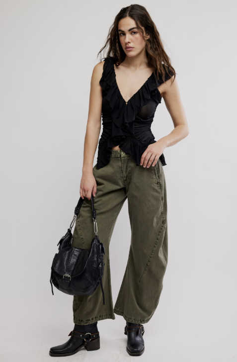 Woman wearing a black ruffled top and green pants with a black bag on a white background
