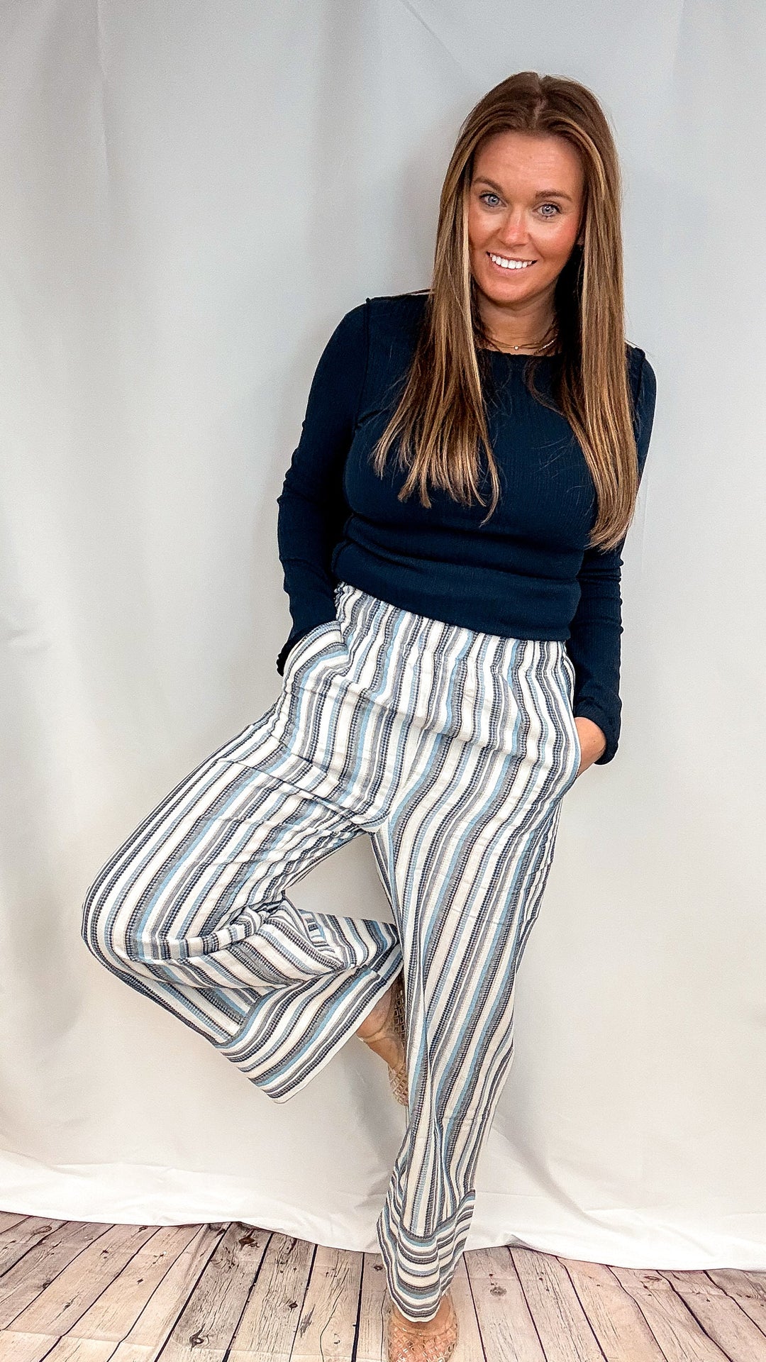 Woman wearing navy long sleeve top and blue stripe pants on plain background