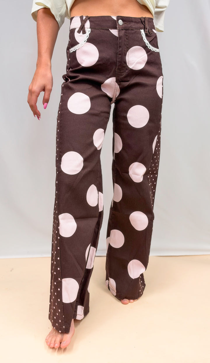 Woman wearing brown pants with large pink polka dots on plain background