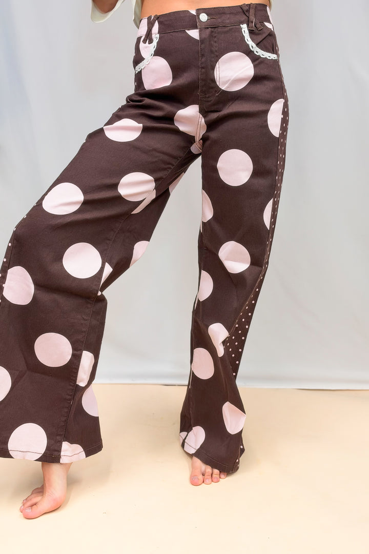Woman wearing brown pants with large light pink polka dots on plain background