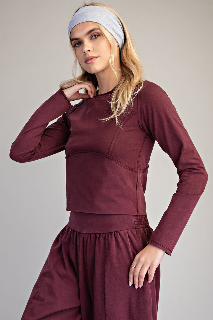A woman modeling a matching burgundy long-sleeve crop top and high-waisted pants set, paired with a light gray headband, against a neutral gray studio background.