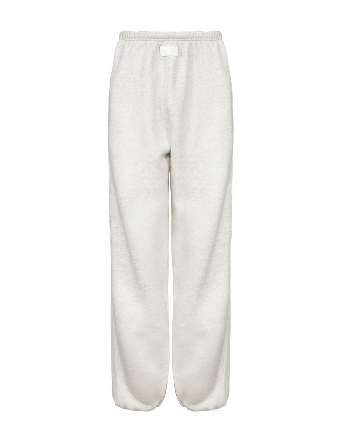 A pair of wide-leg sweatpants in a soft, textured off-white fabric, featuring an elastic waistband and a small white rectangular label at the center front, shown against a plain white background.