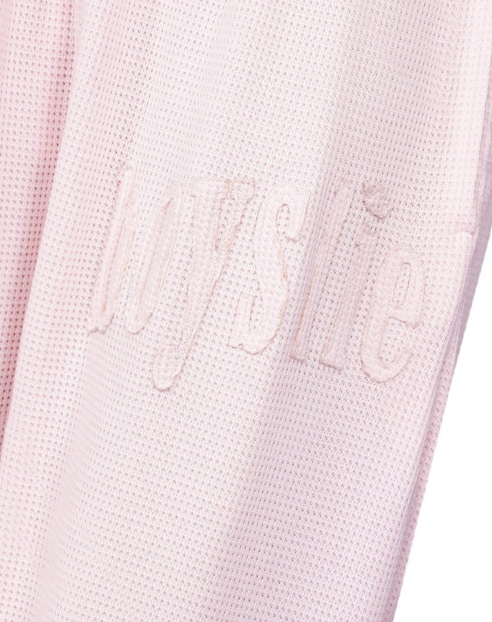 Close-up of a light pink mesh garment with tonal embroidered script text reading &