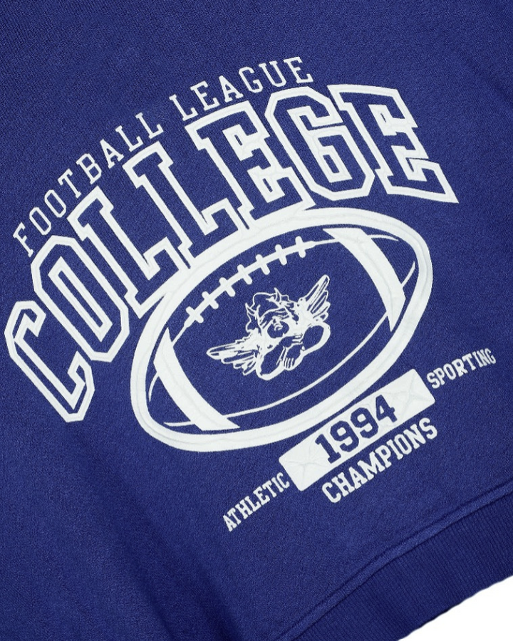 Close-up of a royal blue sweatshirt featuring a white collegiate football graphic with the text &