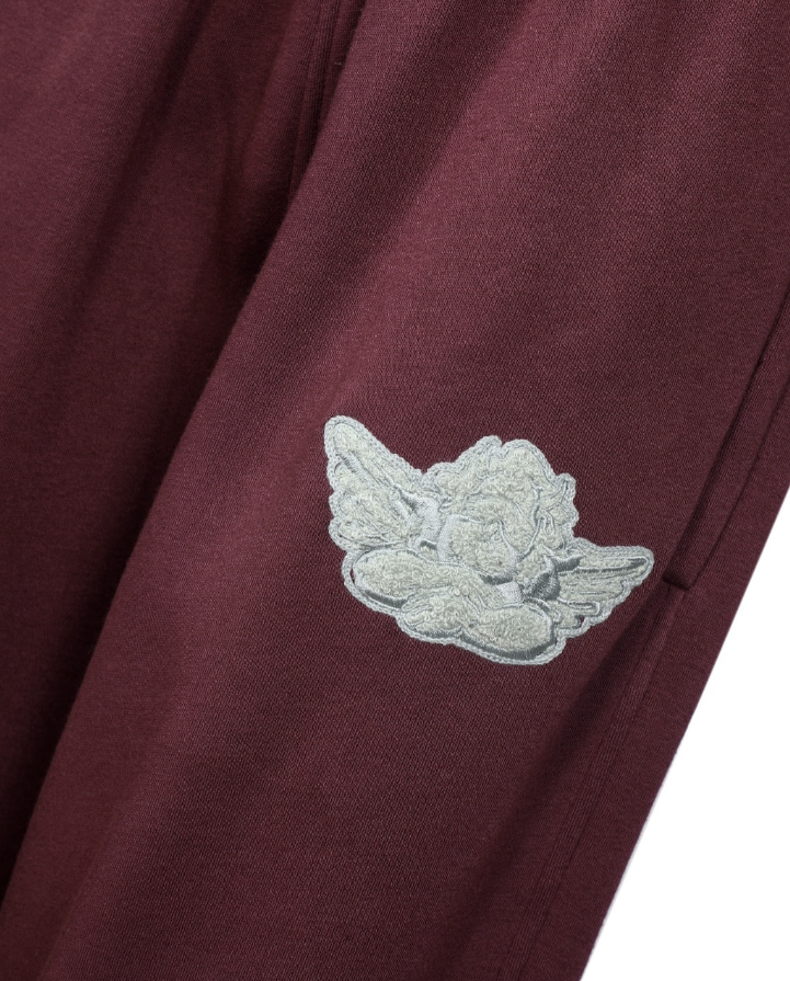 A close-up of a maroon fabric garment featuring a light gray embroidered angel motif on the upper left sleeve.