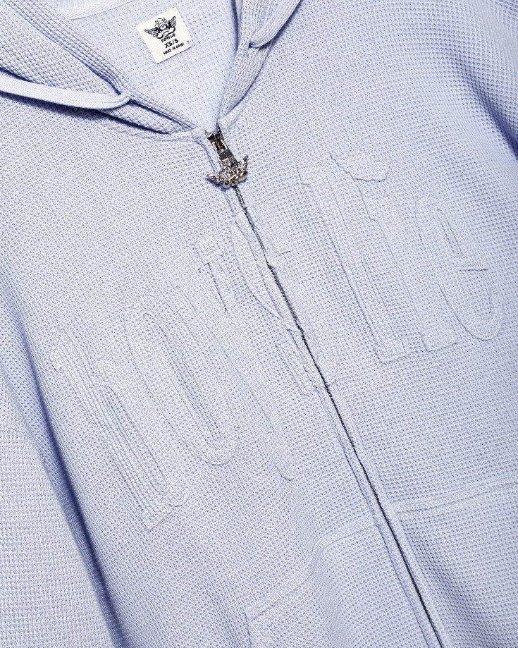 Close-up of a textured light lilac hoodie with a brand label on the hood.