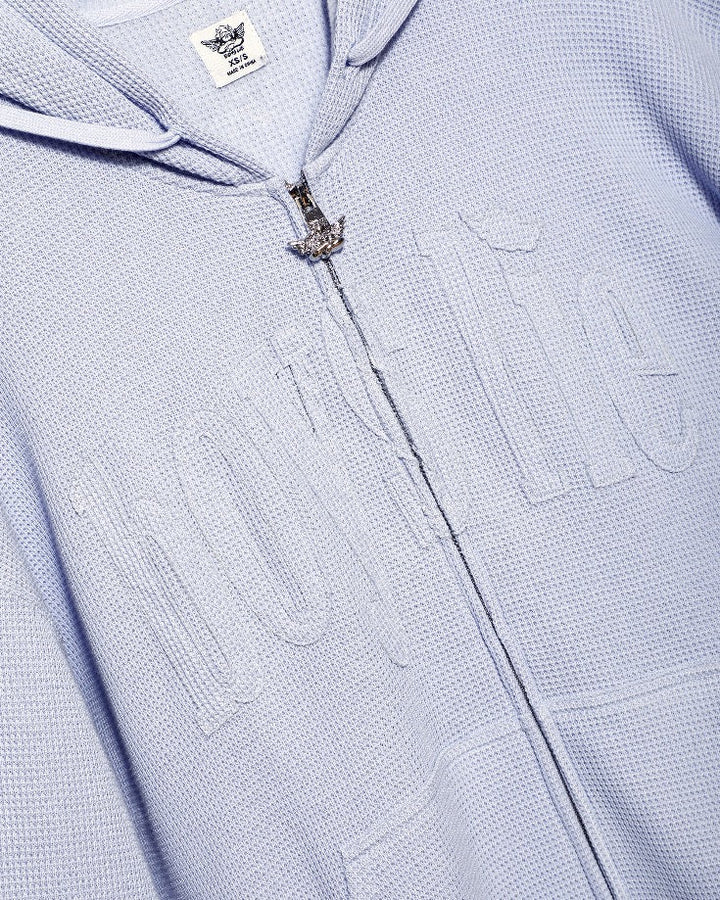 Close-up of a textured light lilac hoodie with a brand label on the hood.