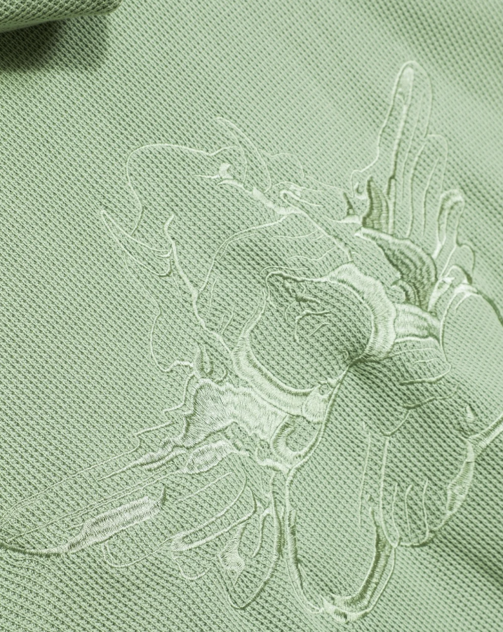Close-up of a light sage green textured fabric with a tonal embroidered floral motif.