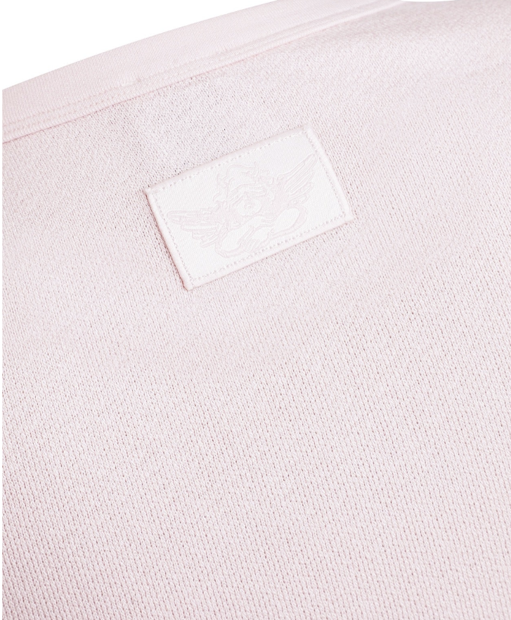 Close-up of a light pink knit fabric with a small white rectangular embroidered patch on the upper left side.