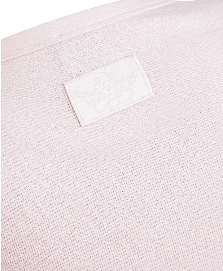 Close-up of a light pink knit fabric with a small white rectangular embroidered patch on the upper left side.