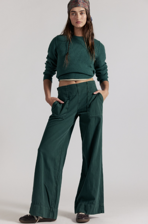 Woman wearing dark green denim pants with matching sweater on white background