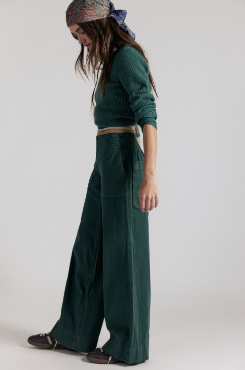 Woman wearing dark green denim pants with matching sweater on white background