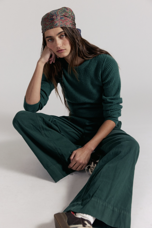 Woman wearing dark green denim pants with matching sweater on white background