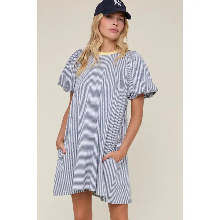 Woman wearing blue striped dress with yellow detail and hat on plain background