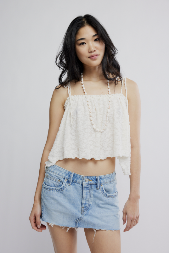 Woman wearing a white lace top and denim skirt on a plain background