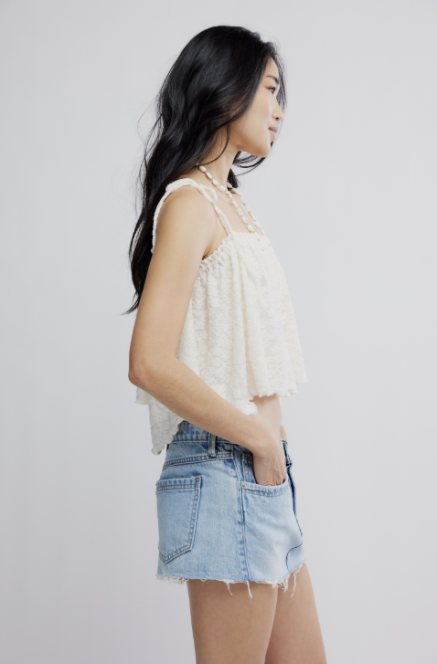 Woman wearing a white lace top and denim shorts on a plain background