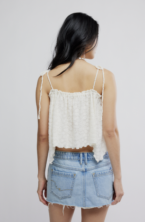Woman wearing a white lace top and denim skirt on a plain background