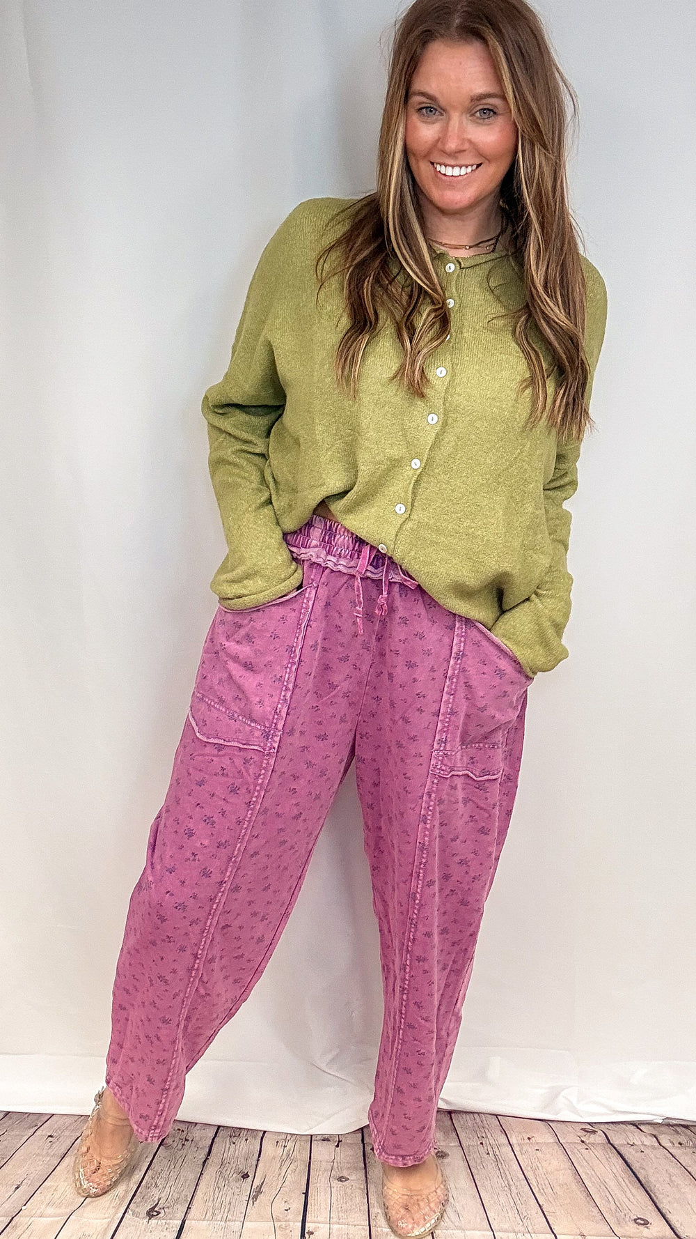 Woman wearing purple floral barrel sweatpants with green knit sweater on white background