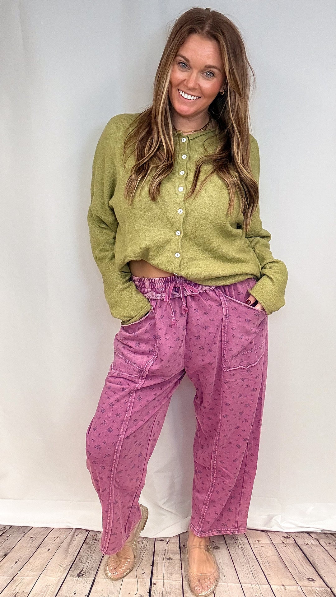 Woman wearing purple floral print barrel sweatpants and green knit sweater on white background