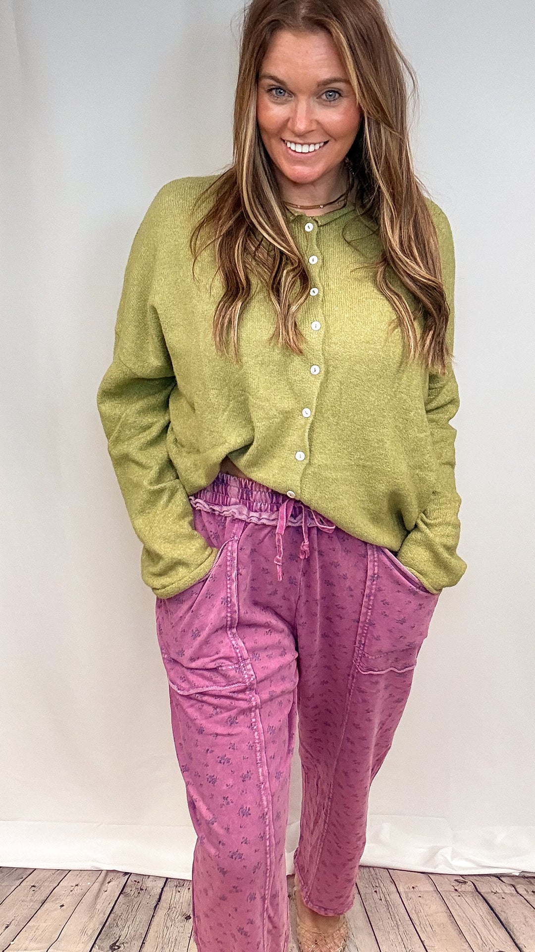 Woman wearing purple floral print barrel sweatpants and green knit sweater on white background