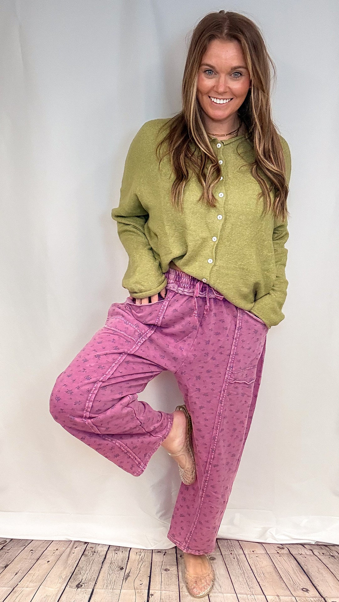 Woman wearing purple floral print barrel sweatpants and green knit sweater on white background