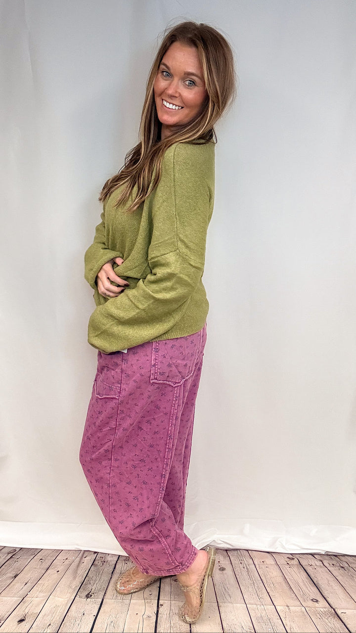 Woman wearing purple floral print barrel sweatpants and green knit sweater on white background