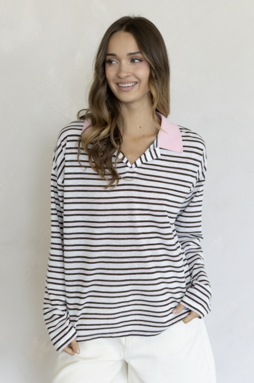 Woman wearing pink and brown stripe collared shirt and white pants on plain background