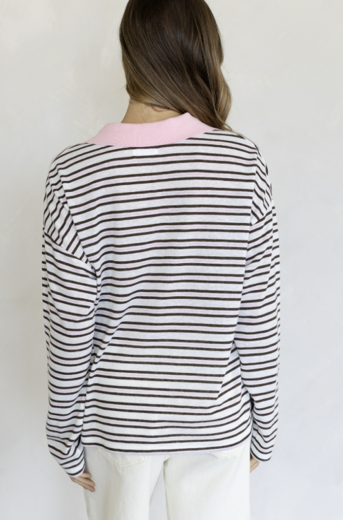 Woman shown from behind wearing brown and pink stripe collared shirt and white pants on plain background