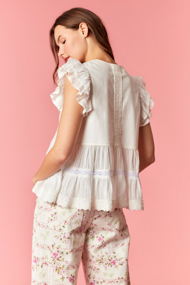 Woman wearing a white ruffled top and floral pants on a pink background